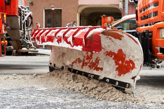 Fragment of a snowplow bucket on the streets of a small European city. Close-up