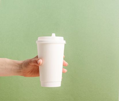 Eco friendly zero waste disposable tableware. Woman hand holding white large takeaway paper coffee cup mock up on green background
