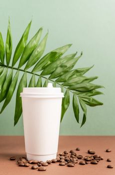 Zero waste and ecology concept. Eco-friendly disposable white paper cup with tropical leaf and coffee beans, mock up design