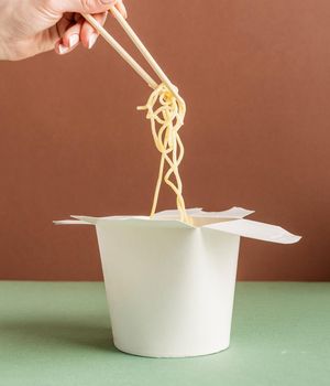 Zero waste and ecology concept..Opened WOK paper box for mock up design. Woman hand holding noodles with chopsticks