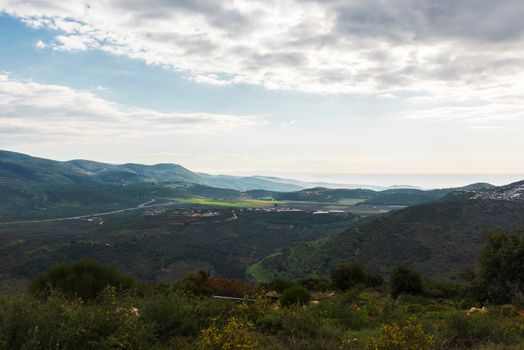 A view of a mountain range and a green valley in the morning at sunrise, against a dramatic backdrop of blue skies and clouds. North District Israel. High quality photo. Travel concept hiking