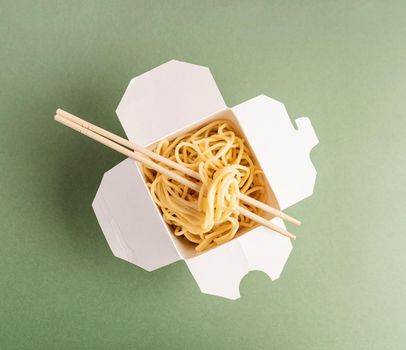 Zero waste and ecology concept. Opened WOK paper box with noodles and chopsticks top view flat lay on green background