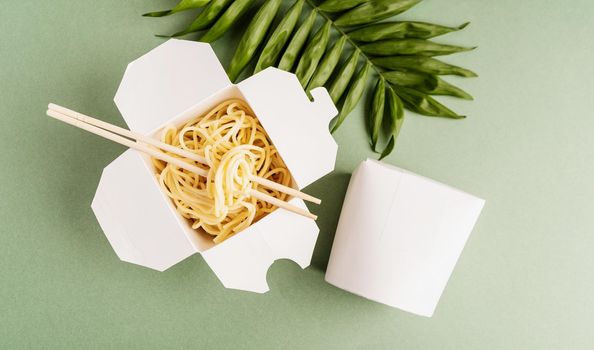 Zero waste and ecology concept. Opened WOK paper box with noodles and chopsticks, mock up design top view flat lay on green background