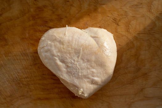 Boiled chicken fillet in the shape of a heart on an old wooden cutting board.