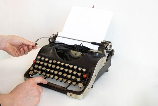 An old typewriter and a blank sheet of paper inserted. Isolated on a white background. The hands of the master set up the typewriter.
