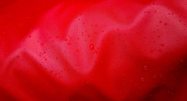 Large drops of water on a red textile with a waterproof effect. Water-repellent impregnation. Texture drops on the fabric.