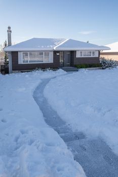 Pathway over front yard leading to average house cleaned from the snow