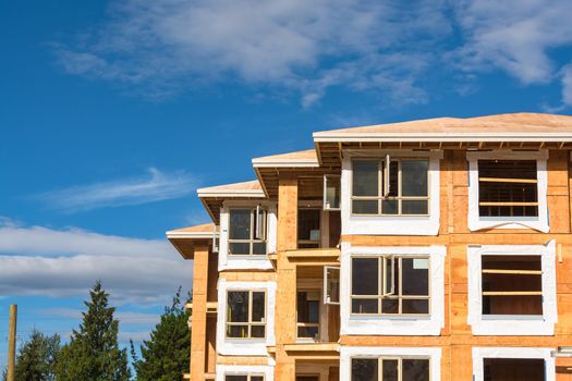 Roof corners, windows, and walls of new aparntment building under construction on blue sky background