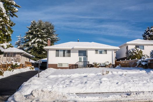 Modest residential house with asphalt driveway and front yard in snow on sunny winter day