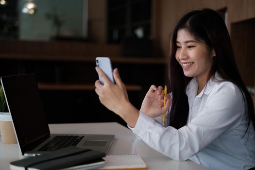 Joyful businesswoman sitting at desk looking at cell phone screen talking with friend make informal video call