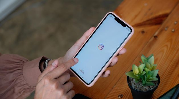 CHIANG MAI, THAILAND - MAR 21 2021 : Woman hand holding iphone with logo of instagram application. Instagram is largest and most popular photograph social networking.