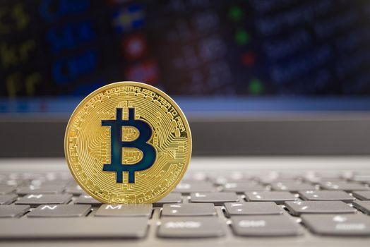 Bitcoin on the computer keyboard in front of the monitors with currency exchange schedules. Digital or virtual currency price increase concept, selective focus