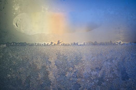 Iridescent glow as the sun strikes a layer of ice or frost on a blue surface in early spring or winter in a concept of the seasons