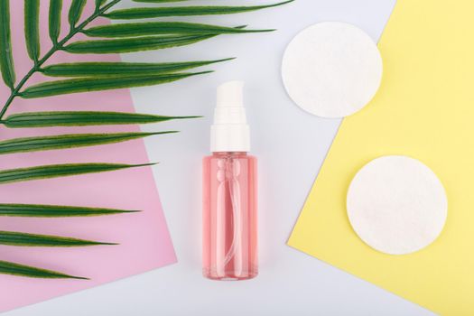 Flat lay with cleansing and soothing foam for make up removing next to cotton pads on pink and yellow pieces of paper and palm leaf. Concept of skin care and make up removing tools