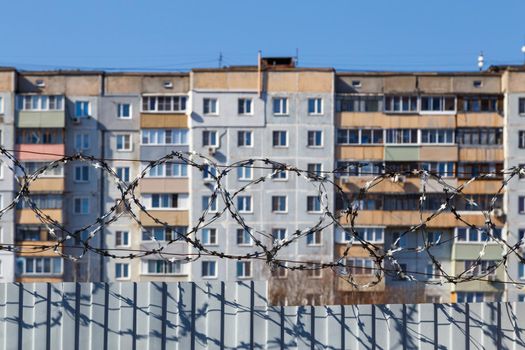 residential multi-storey building behind a fence with barbed wire at daylight, the concept of imprisonment, restriction of freedom, quarantine.