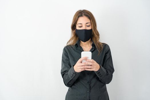 Studio shot of serious young model woman in business shirt clothes isolated on white copy space background looking at smartphone wearing medical protection mask. Stress for Covid-19 data news concept