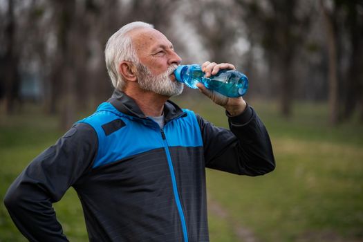 Senior man is drinking water after exercising in park.