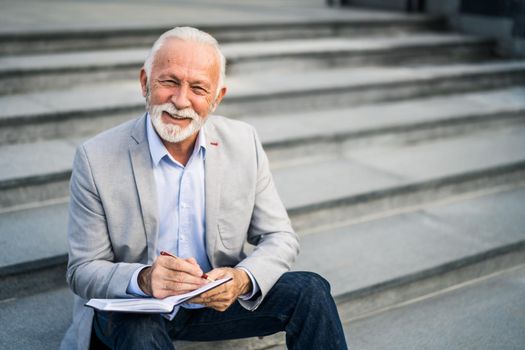 Happy senior businessman is writing his schedule.