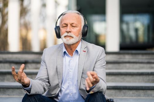 Happy senior businessman is meditating after work in front of company building.