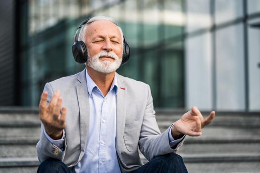 Happy senior businessman is meditating after work in front of company building.