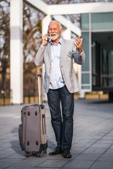 Happy senior businessman is arriving from business trip. He is talking on phone.