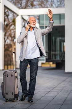 Senior businessman is arriving at bus station. He is calling taxi.