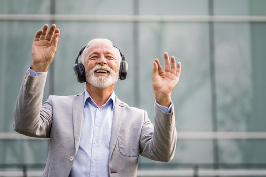 Outdoor portrait of senior businessman who is enjoying music on headphones.