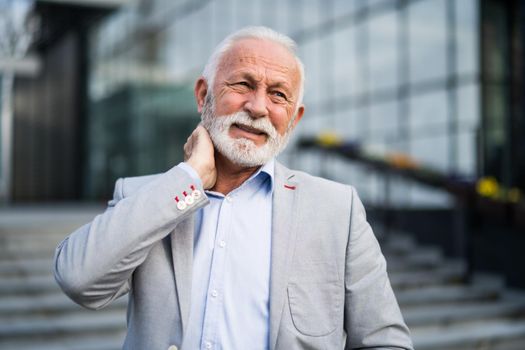 Senior businessman is having sprain in neck in front of company building.