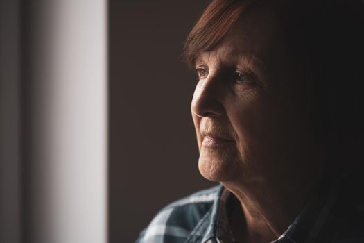 Portrait of lonely senior woman who is looking through window.