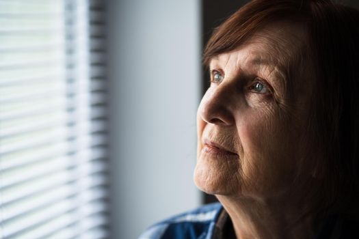 Portrait of lonely senior woman who is looking through window.