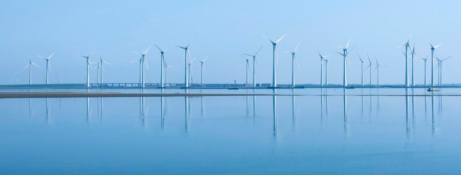 wind turbines reflected in water near philipsdam in dutch province of zeeland under blue sky