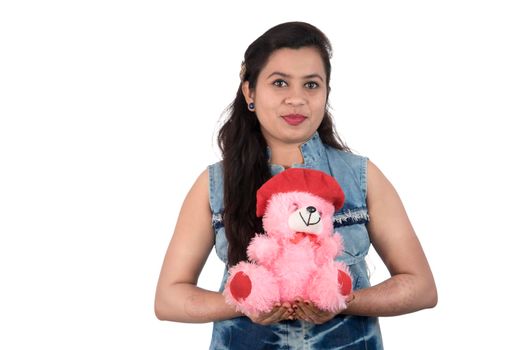 Beautiful young girl holding and playing with a teddy bear toy on a white background.