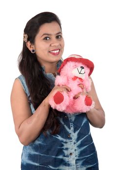 Beautiful young girl holding and playing with a teddy bear toy on a white background.