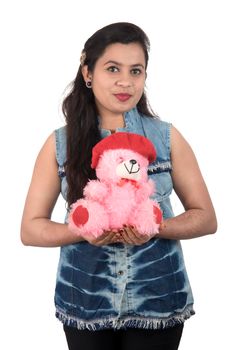 Beautiful young girl holding and playing with a teddy bear toy on a white background.