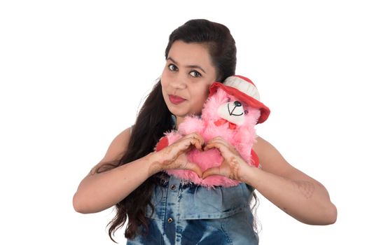 Beautiful young girl holding and playing with a teddy bear toy on a white background.