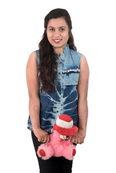 Beautiful young girl holding and playing with a teddy bear toy on a white background.