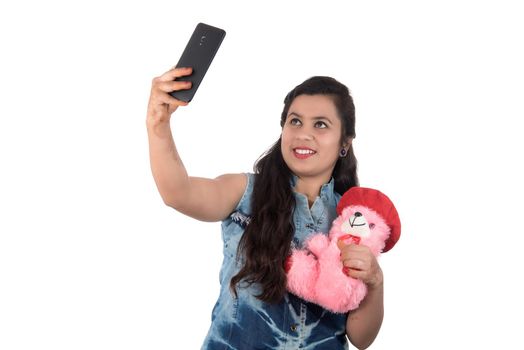 Woman taking picture or selfie with mobile phone and holding teddy bear