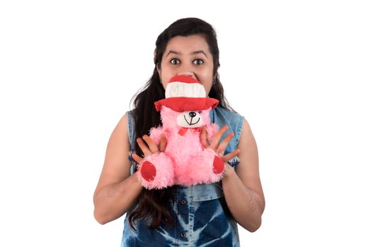 Beautiful young girl holding and playing with a teddy bear toy on a white background.