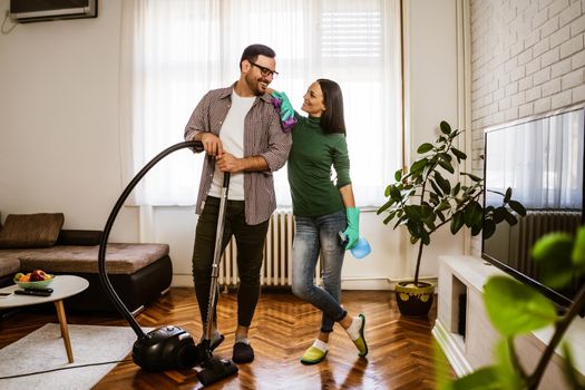 Young happy couple is cleaning their apartment.