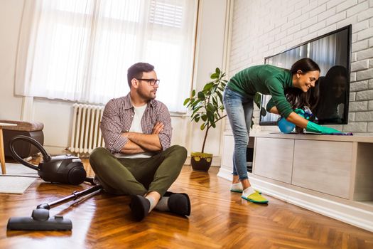 Man is lazy. His wife is telling him to continue cleaning their apartment.