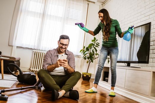 Man is lazy. His wife is telling him to continue cleaning their apartment.