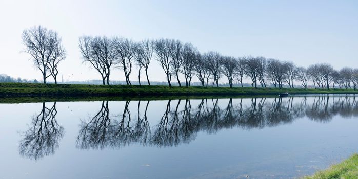 trees reflected in water of canal near middelburg in dutch province of zeeland with small boat