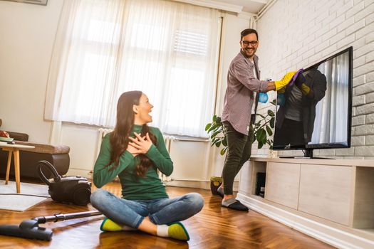 Young happy couple is cleaning their apartment.