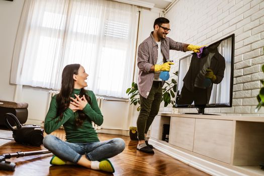 Young happy couple is cleaning their apartment.