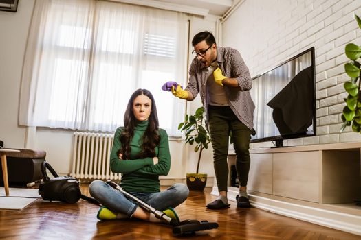Woman is lazy. Man is telling her to continue cleaning their apartment.