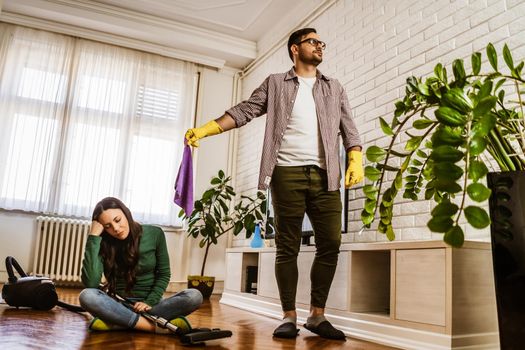 Woman is lazy. Man is telling her to continue cleaning their apartment.