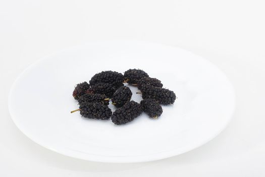 White plate with ripe mulberries on a white background