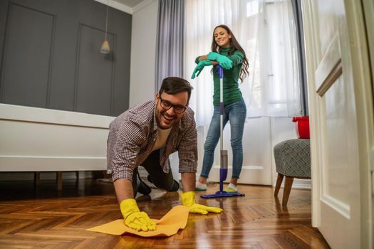 Young happy couple is cleaning their apartment.