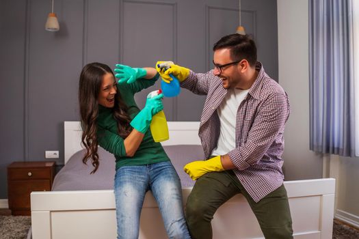 Young happy couple is having fun while cleaning their apartment.