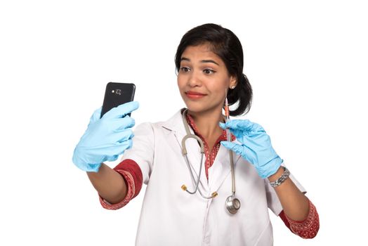 Female doctor taking selfie with stethoscope and injection by smartphone on white background.